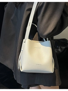 White litchi pattern bucket bag with wide shoulder strap worn by a model in a suit