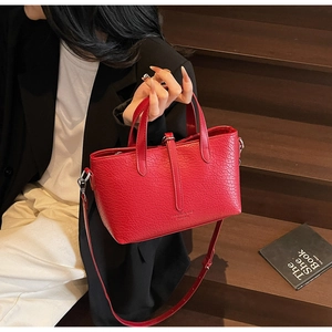 Detail of red pebbled leather handbag with silver hardware and gold logo on stairs