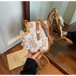Detailed view of cream bear print crossbody phone bag with brown leather trim and bear charm