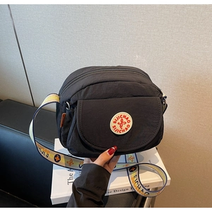 Detailed shot of a black nylon shoulder bag with a colorful floral jacquard strap and badge