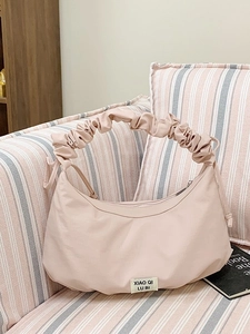 Rosafarbene geraffte Croissant-Handtasche auf einem Sofa mit gefaltetem Wolkengriff