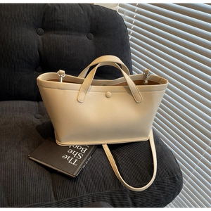 Detail of beige lychee grain leather handbag on a black corduroy chair background