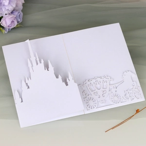 Detail of laser-cut white wedding invitation with intricate castle and horse carriage