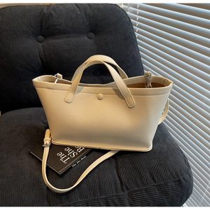 Detail of a beige leather bucket bag with silver hardware on a black corduroy chair