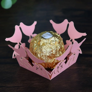 Detail of pink laser-cut paper favor box with bird silhouette and lace edge for weddings