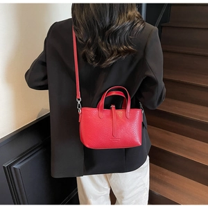 Detailed view of red textured leather handbag with silver rings and detachable strap