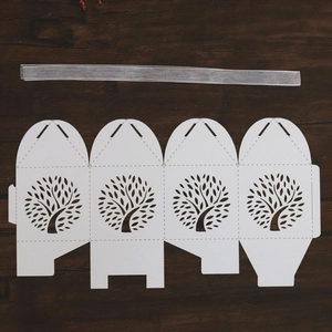 Flat lay of laser-cut Tree of Life wedding favor box template with silver silk ribbon