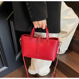 Detail of red crocodile texture tote bag with cylindrical handles and adjustable strap
