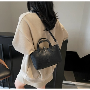 Detail of black textured leather handbag worn crossbody by a model in a modern setting
