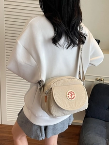 Minimalist beige nylon crossbody bag with wide logo strap worn by woman in white hoodie
