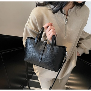 Detail of a black faux leather handbag with crocodile texture and double top handles