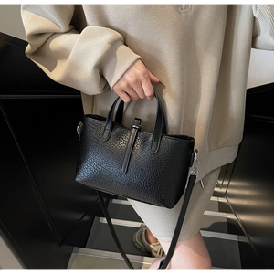 Model wearing a black crocodile-patterned crossbody bag against a minimalist staircase