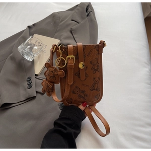 Detail of brown leather phone bag with teddy bear print and cute bear charm