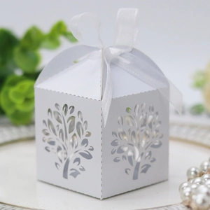 Detailed view of white laser-cut favor box with tree patterns and white organza ribbon