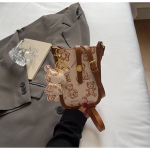 Detail view of mini cream phone bag with brown bear print and matching plush bear charm