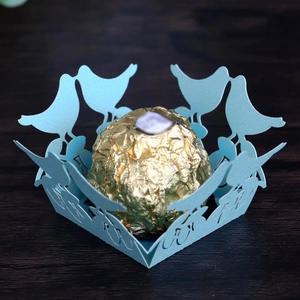 Detail of light blue laser-cut paper chocolate tray with delicate bird lace design