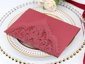 Detail of burgundy laser cut lace wedding invitation card on elegant ceramic plate