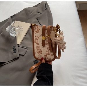 Detail of cream crossbody phone bag with brown bear print and matching bear charm