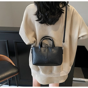 Close-up of textured black leather handbag with crossbody strap on minimalist background