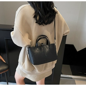 Detail of black embossed leather handbag worn over the shoulder by a model