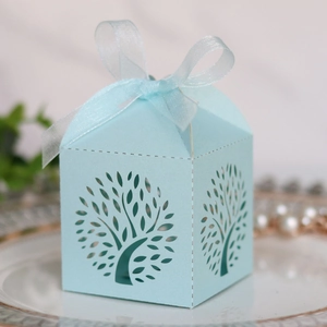 Detail of light blue laser-cut candy box with tree pattern and chiffon ribbon on a ceramic plate