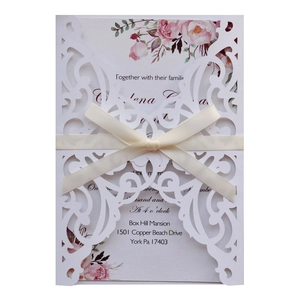 Elegant white laser-cut wedding invitation with cream ribbon bow and floral inner page