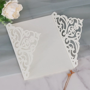 Detail of laser-cut cream pearlescent paper invitation with intricate floral lace patterns