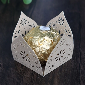 Detail showing beige laser-cut lace candy box with floral patterns on wooden texture