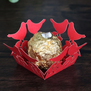Macro shot of a red laser-cut wedding favor box with bird patterns and golden chocolate