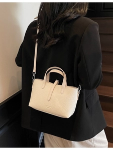 Elegant off-white leather handbag with cross-body strap shown on model in black blazer