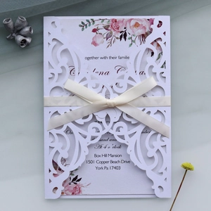 Detailed laser-cut wedding invitation with white floral envelope and silk ribbon bow