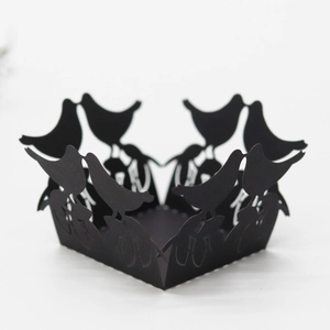 Detail of laser-cut black paper cupcake wrapper featuring intricate flying bird silhouette