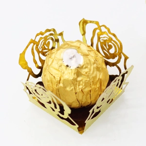 Détail macro d'une boîte à dragées dorée découpée au laser avec motif de rose et chocolat