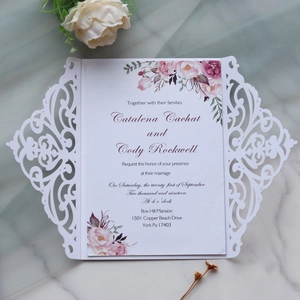 Detail of laser cut white wedding invitation with floral insert on marble surface