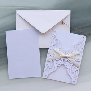 Detail of laser-cut floral wedding invitation with purple card and silk ribbon bow