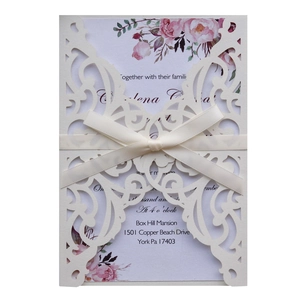 Detail of laser-cut off-white wedding invitation with pink roses and satin ribbon bow