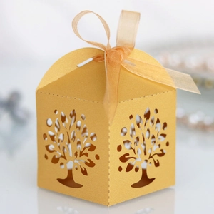 Macro detail of laser-cut tree pattern on gold paper favor box with organza ribbon