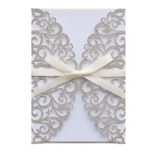 Macro detail of laser-cut silver glitter wedding invitation with white satin ribbon bow