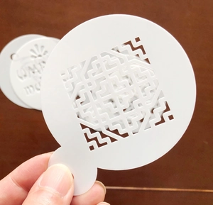 Detail of PET laser-cut cake stencil featuring a geometric maze pattern with a small handle