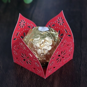 Detailed laser cut red paper candy box with floral lace pattern on wooden surface