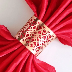 Rose gold metal napkin ring with hollow geometric carving on a red satin napkin