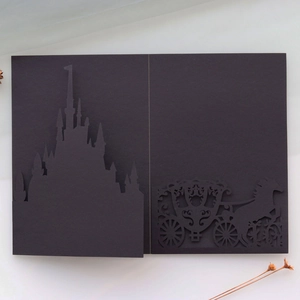 Close-up of laser-cut black castle and carriage wedding invitation with intricate details