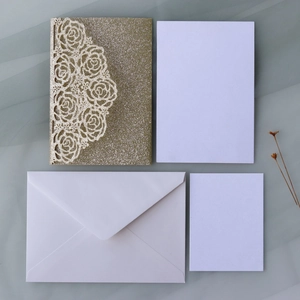 Detail of laser-cut gold glitter rose invitation set with white envelopes and cards