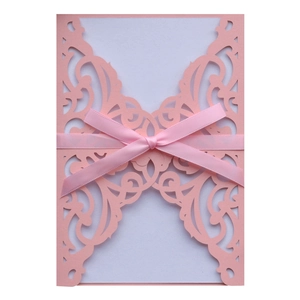 Detail of pink laser-cut wedding invitation with elegant scroll patterns and satin ribbon