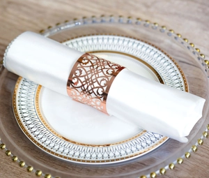Rose gold laser-cut metal napkin ring with floral pattern on white satin cloth