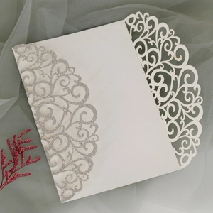 Detail view of laser-cut wedding invitation with white vine pattern and silver glitter accents