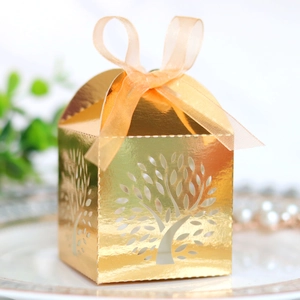 Detail of laser-cut tree pattern on golden wedding favor box with orange ribbon