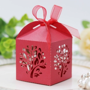 Detail of red laser-cut candy box with tree pattern, ribbon bow, and wedding decorations