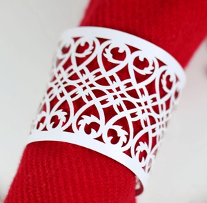 Detail of white laser-cut napkin ring with intricate vine patterns on red fabric