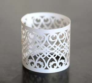 Detail of white laser-cut napkin ring with intricate floral vine hollowed patterns